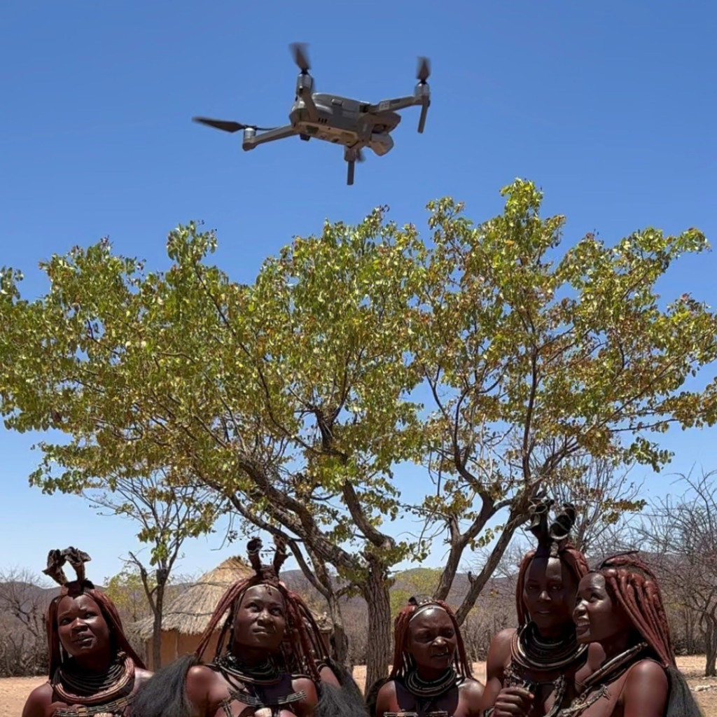 Eine Drohne fliegt über die Köpfe einer Gruppe Ovahimba-Frauen hinweg.