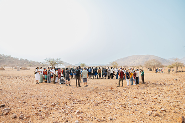 Eine Menschengruppe steht im Kreis inmitten der namibischen Savanne.