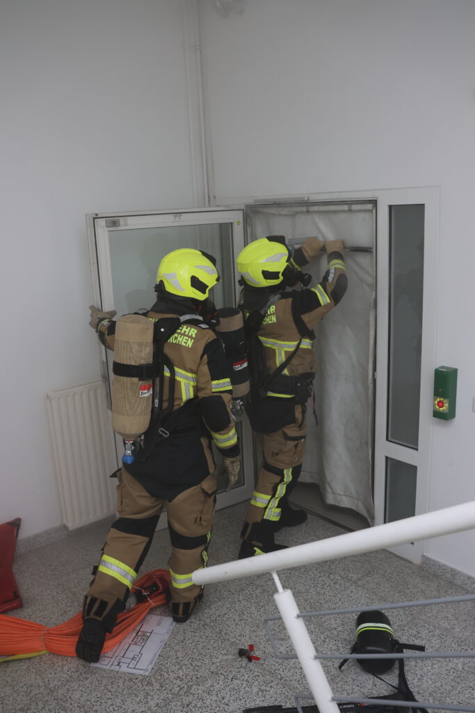 Zwei Feuerwehleute setzen Rauchschutztür ein.
