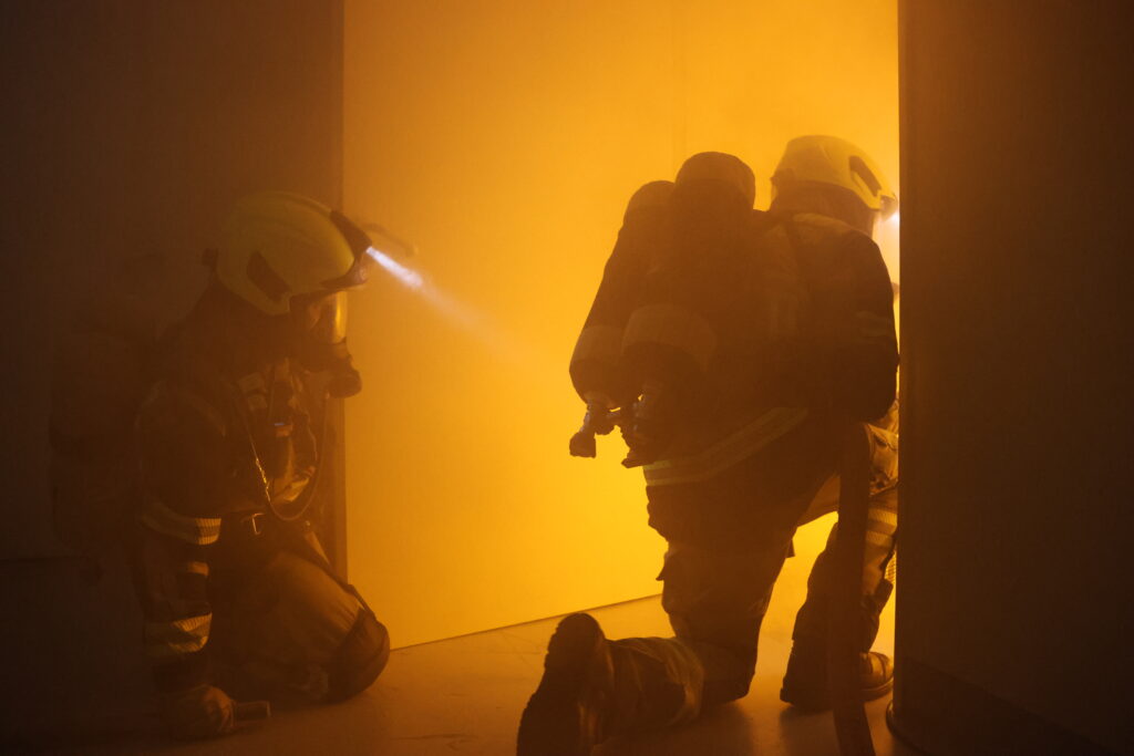 Feuerwehrleute auf verrauchtem Flur bei orangenem Licht
