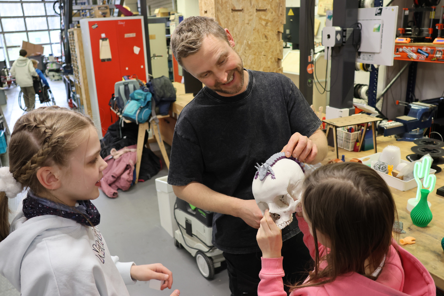 Schülerinnen schauen sich gemeinsam mit Lukas Rauer vom Makerspace einen Totenkopf an.