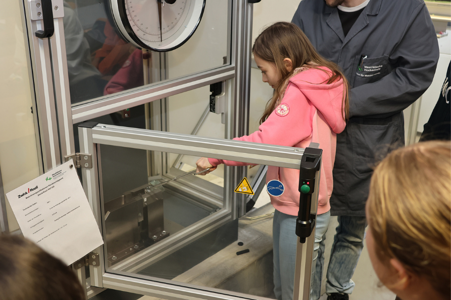 Schülerin nimmt mit einer Zange ein Werkstück aus einem Teststand.